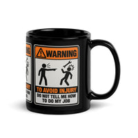 Don't Tell Me How to Do My Job black glossy mug, 11 oz, the WARNING safety-sign placard facing forward with the handle at right, studio view