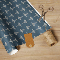 Medical Caduceus Wrapping Paper, white glossy finish: embroidered-look caduceus pattern on an ocean-toned ground, unrolled on a wooden table with scissors, twine and a kraft gift tag