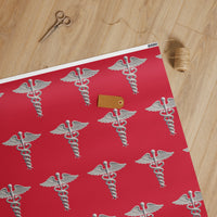 Medical Caduceus Wrapping Paper, caduceus symbols on crimson: white glossy finish, unrolled on a wooden table with scissors, twine and a kraft gift tag